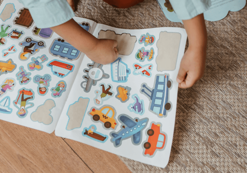Bambino che gioca con un libro di adesivi colorati a tema trasporti.