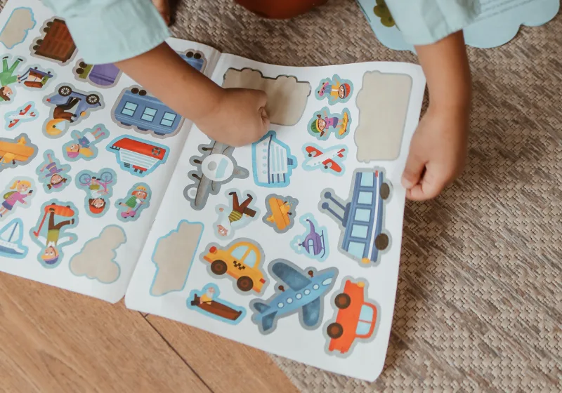 Bambino che gioca con un libro di adesivi colorati a tema trasporti.