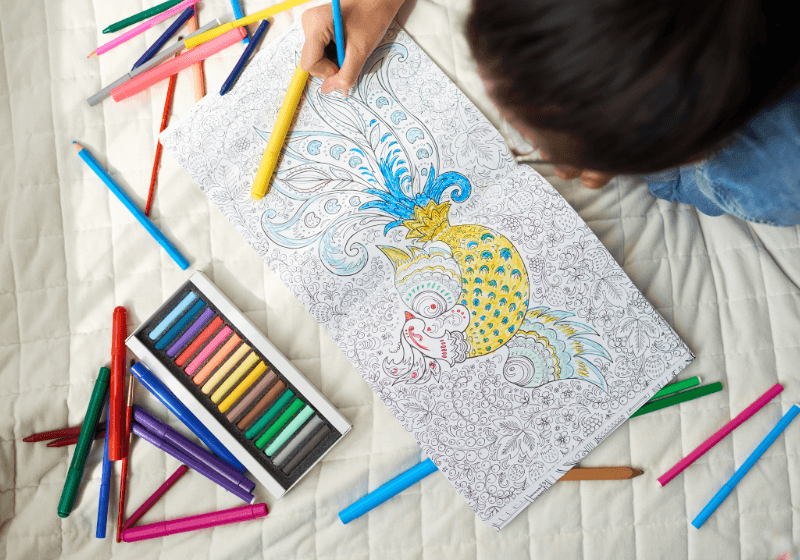 Libri da colorare per bambini. Bambino che colora un libro con disegni dettagliati, circondato da matite colorate e pastelli.